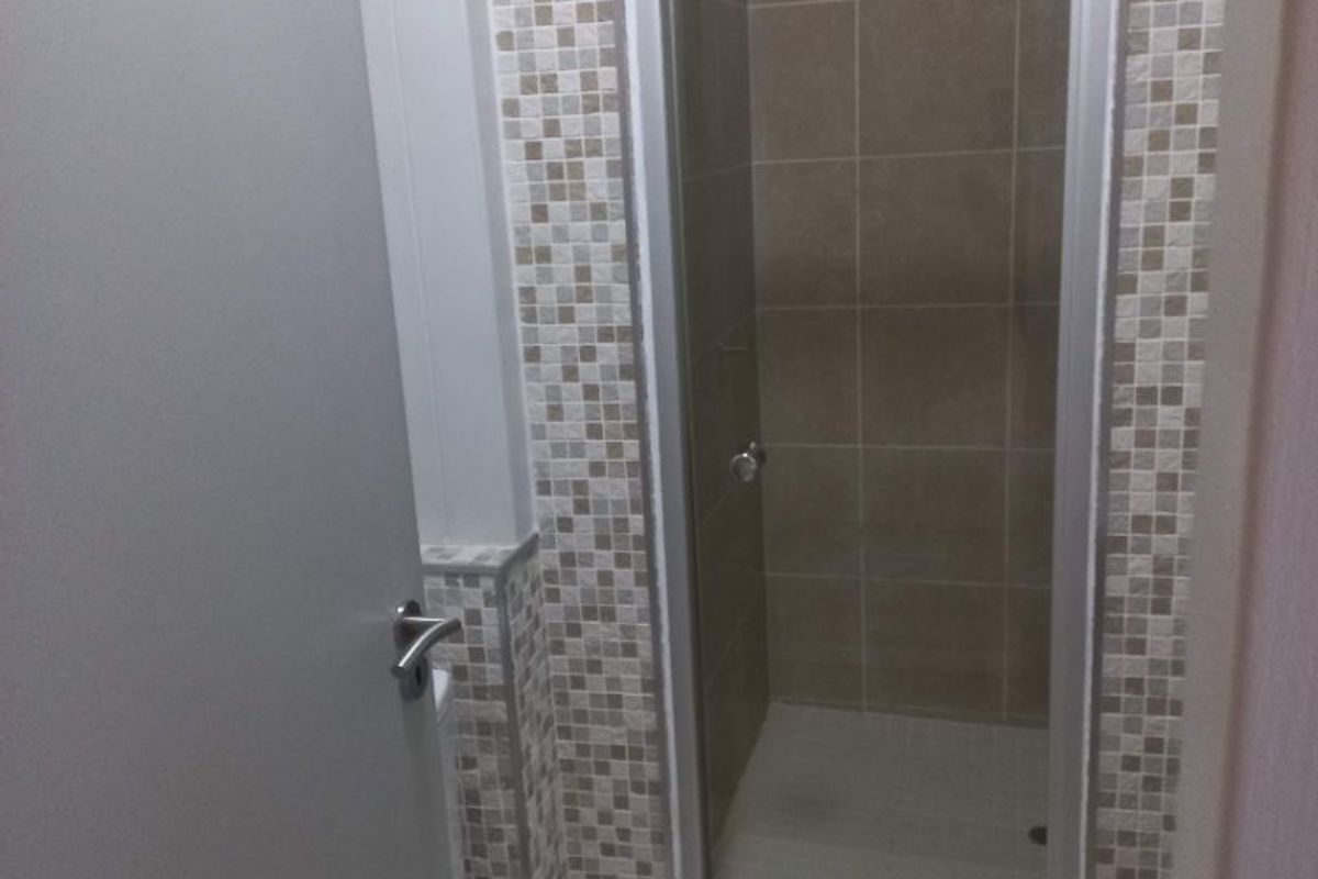 A clean bathroom featuring a glass-enclosed shower with a combination of mosaic and large format neutral-toned wall tiles.