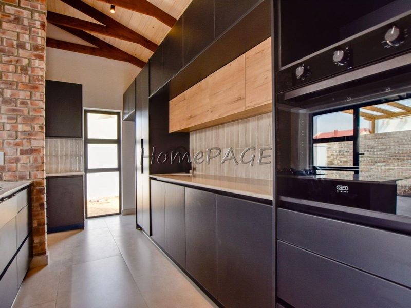 Modern kitchen featuring sleek dark cabinetry, light wood accents, exposed brickwork, timber ceiling beams, and high-quality built-in appliances.
