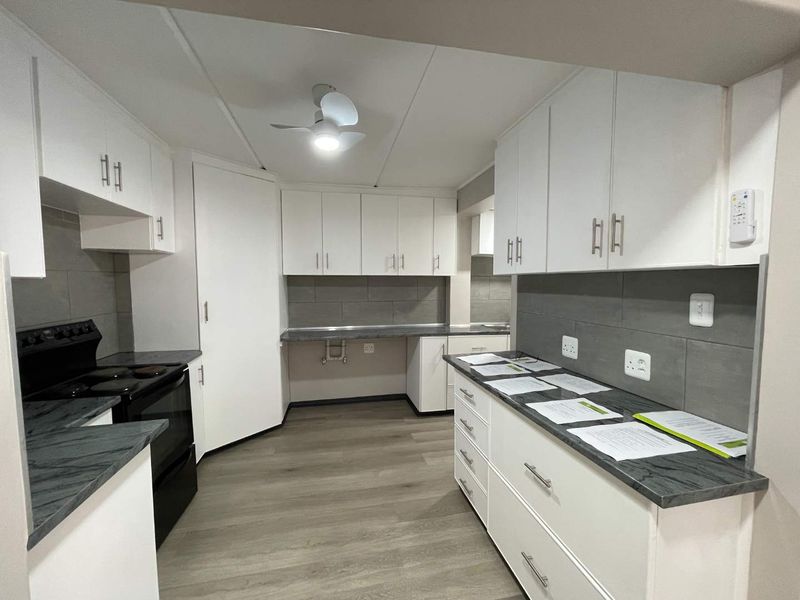 A clean, modern kitchen featuring white cabinetry, dark laminate countertops, grey tiled backsplash, and durable laminate flooring.