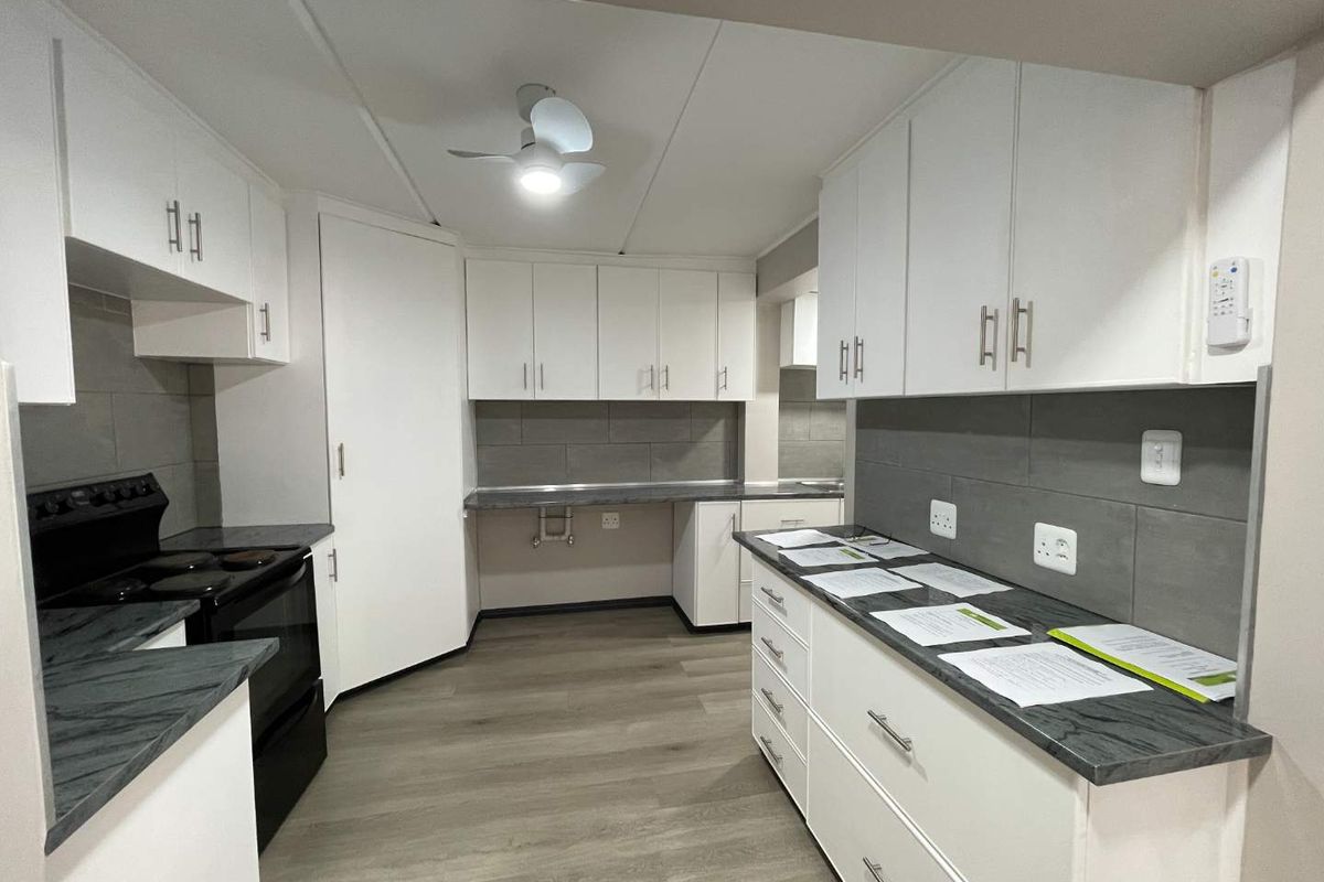 A clean, modern kitchen featuring white cabinetry, dark laminate countertops, grey tiled backsplash, and durable laminate flooring.