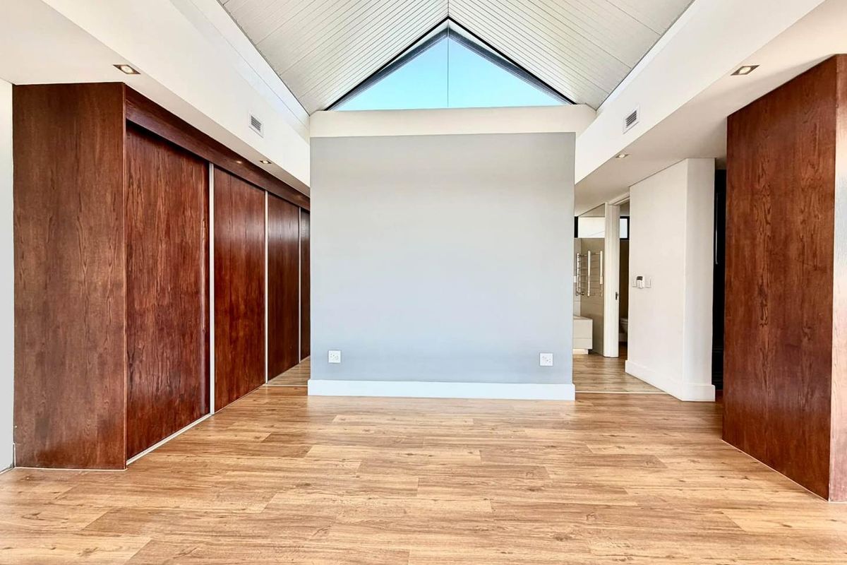 Spacious bedroom featuring high vaulted ceilings, extensive built-in wooden cabinetry, modern laminate flooring, and a unique triangular clerestory window for natural light.