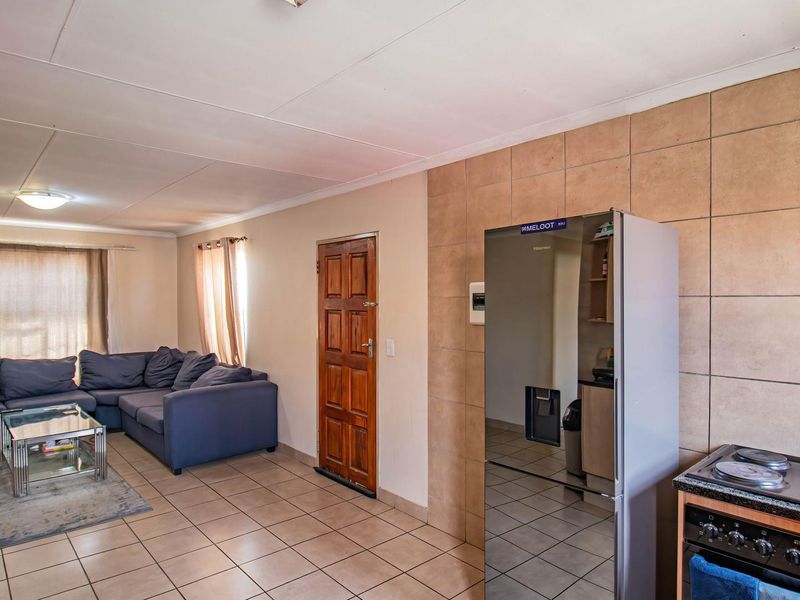 Open-plan living area featuring tiled flooring, a tiled feature wall, and a built-in stove, creating a functional and connected space.