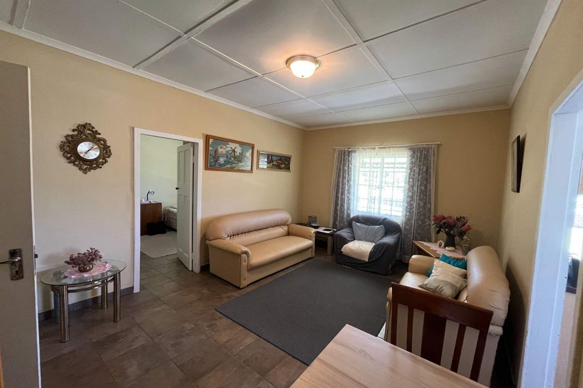 A living room featuring tiled flooring and a tiled ceiling, providing a functional space with access to an adjacent bedroom.