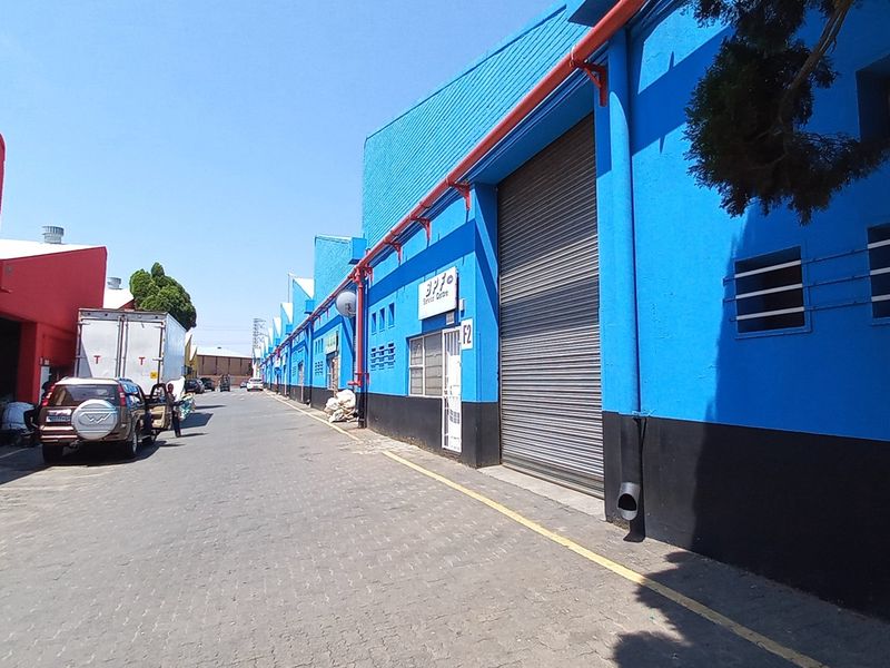 Exterior view of an industrial complex featuring multiple warehouse units with roller shutter doors and vibrant blue and red painted facades.