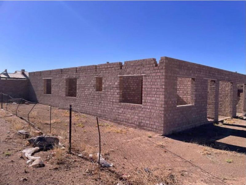 An unfinished residential structure showing exposed brick masonry walls with open window and door frames, requiring significant completion work.