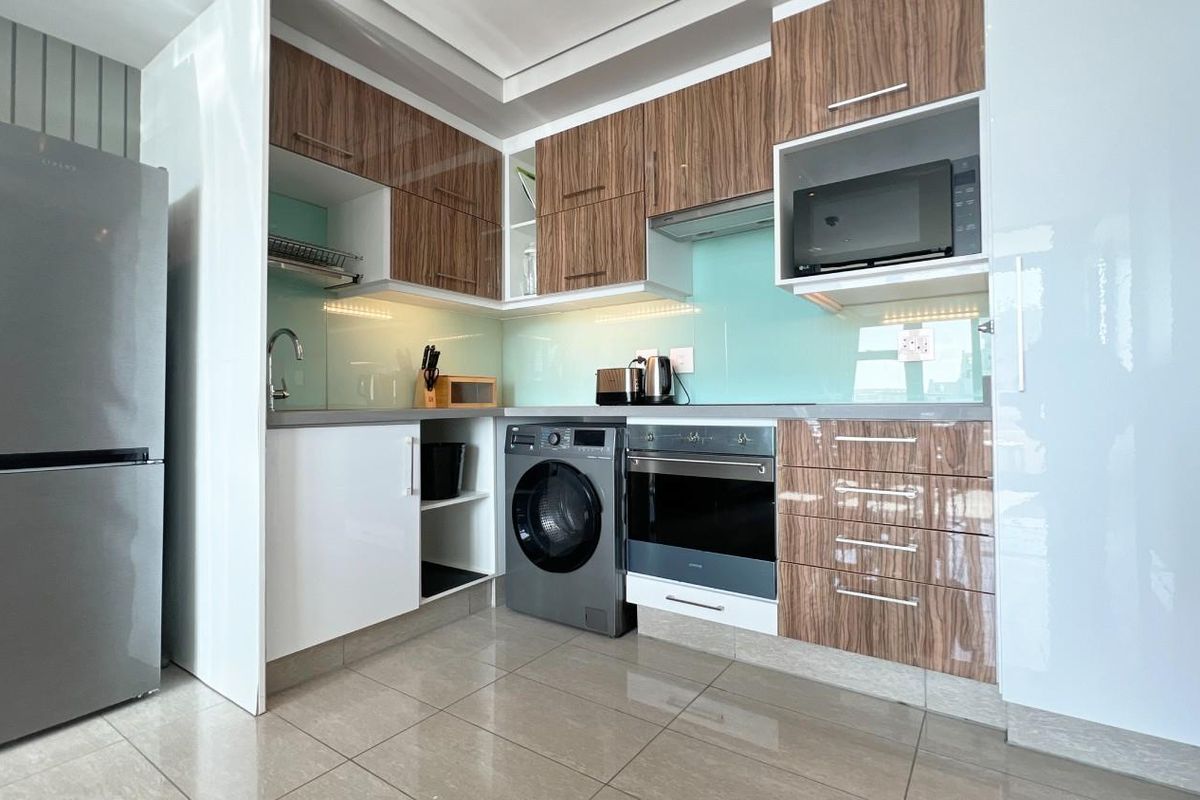 Modern compact kitchen featuring wood-grain and white cabinetry, integrated oven, hob, extractor fan, built-in microwave, and tiled flooring.
