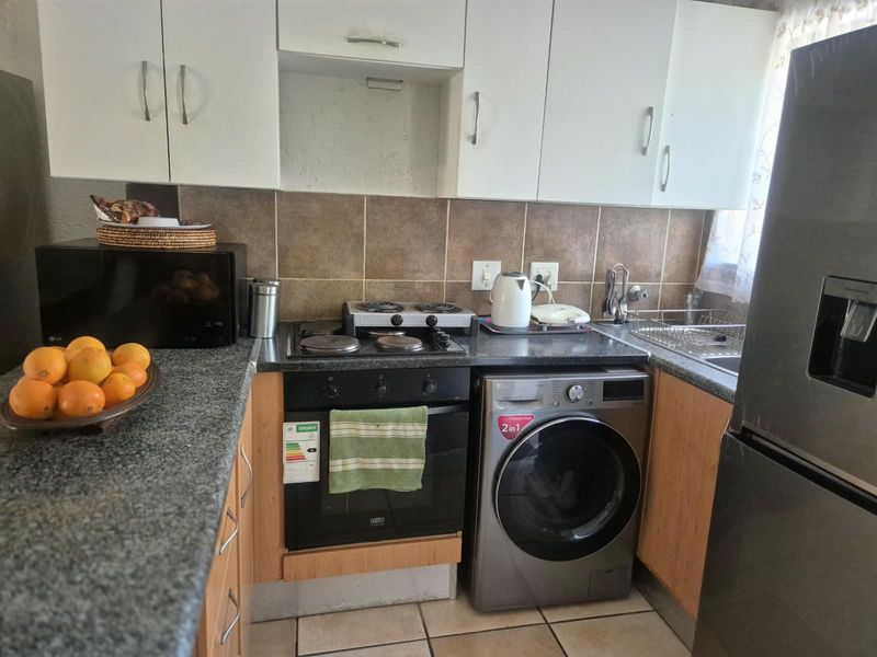 Compact kitchen featuring built-in cabinetry, granite countertops, tiled backsplash, electric hob, oven, and integrated laundry appliance space.