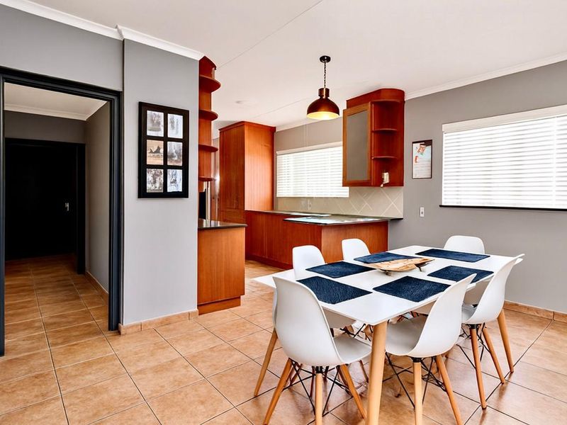 Open-plan kitchen and dining area featuring warm wooden cabinetry, tiled flooring, and natural light through venetian blinds.