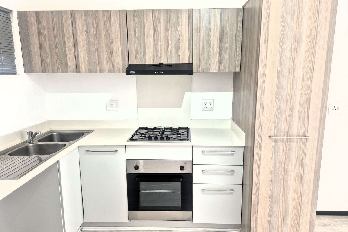 Modern kitchen featuring light wood-grain cabinetry, stone countertops, a gas hob, built-in oven, and a stainless steel double sink.