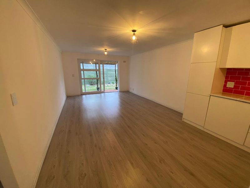 Spacious open-plan living area featuring modern laminate flooring, built-in kitchen cabinetry with a vibrant red backsplash, and sliding doors leading to the garden.