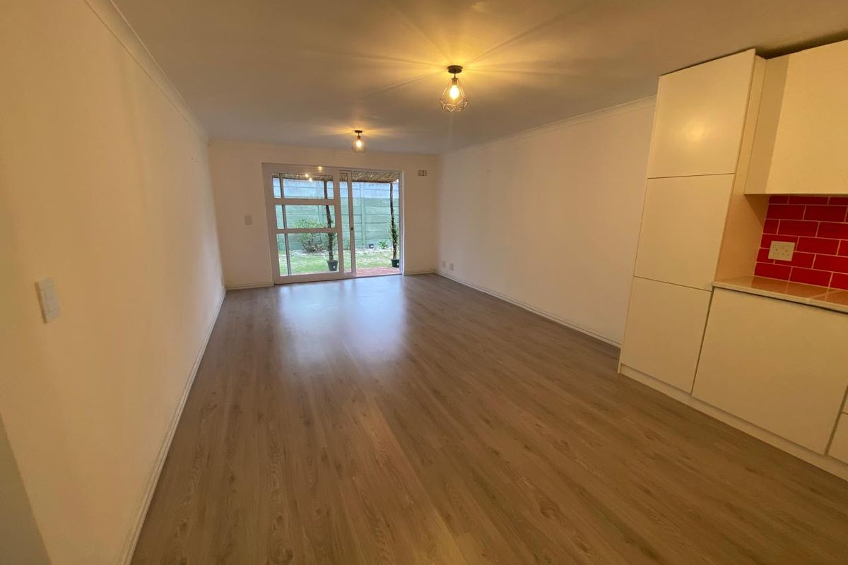Spacious open-plan living area featuring modern laminate flooring, built-in kitchen cabinetry with a vibrant red backsplash, and sliding doors leading to the garden.