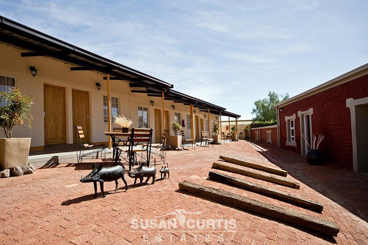 A paved courtyard area featuring a row of hotel guest room entrances with covered walkways and rustic exterior finishes.