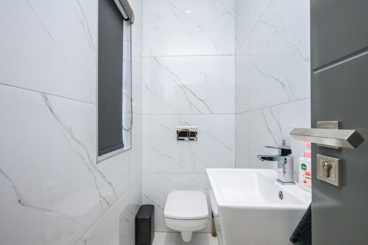 Modern guest bathroom featuring marble-effect wall tiling, a wall-mounted toilet with concealed cistern, and a contemporary basin with a sleek mixer tap.