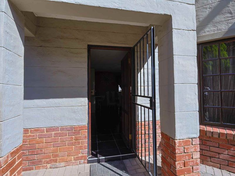 Entrance area of the townhouse featuring a security gate, brick and plaster facade, and tiled threshold.