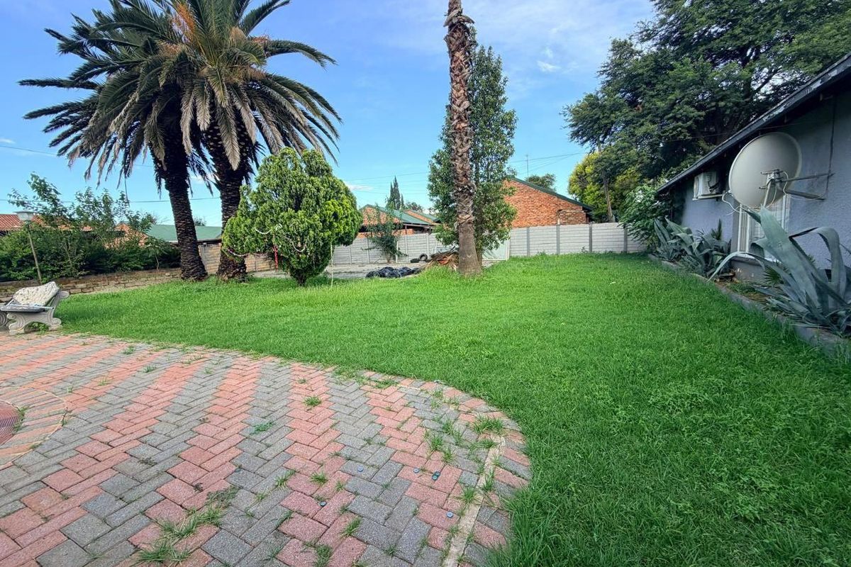 A spacious rear garden featuring a paved patio area, established palm trees, and perimeter walling, offering a private outdoor space.