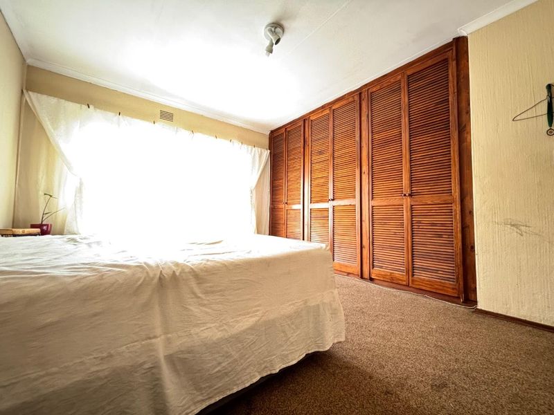 Bedroom featuring built-in wooden louvered wardrobes, carpeted flooring, and natural light from a large window.