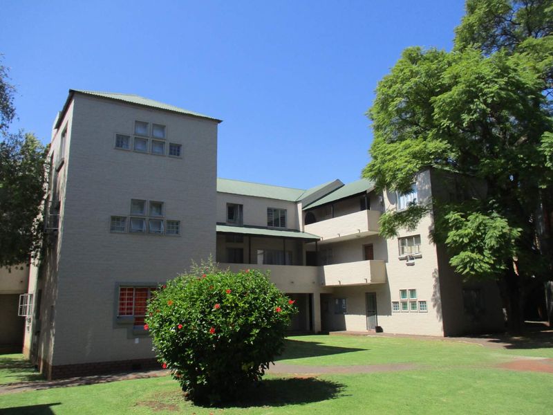 A view of the rear elevation of a multi-story apartment complex featuring a shared lawn, balconies, and established trees.