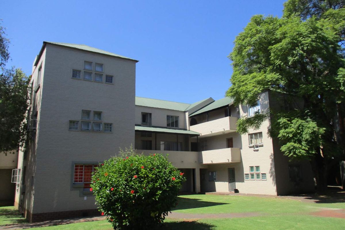A view of the rear elevation of a multi-story apartment complex featuring a shared lawn, balconies, and established trees.