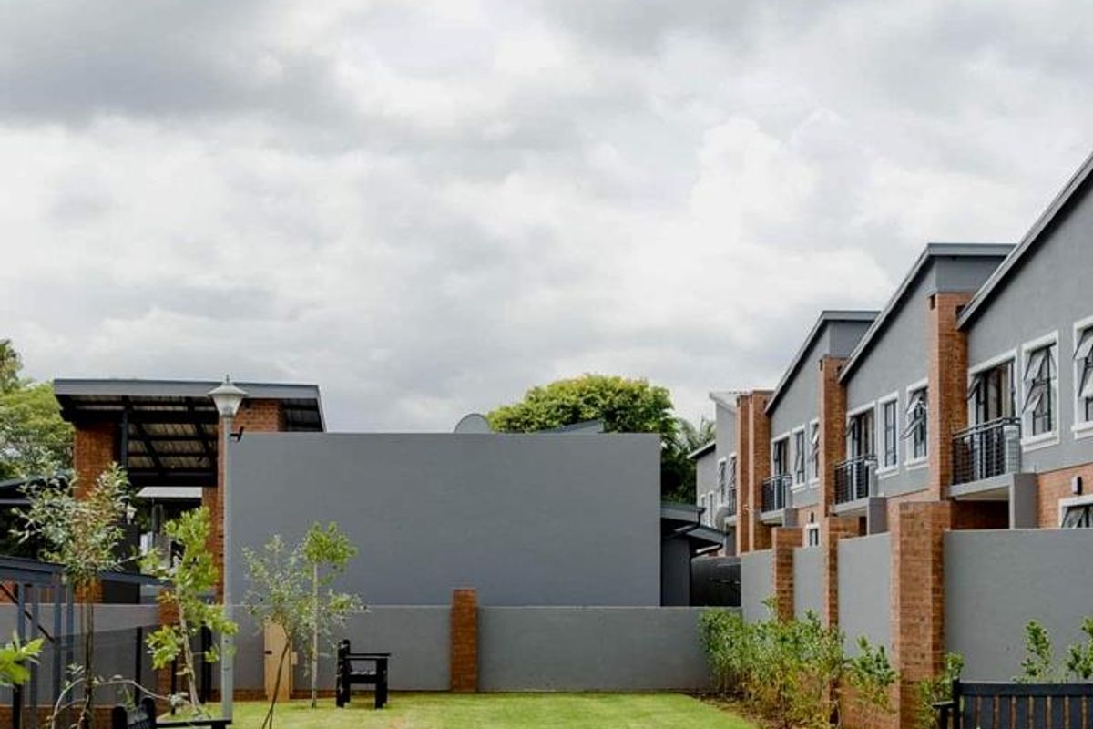 A well-maintained communal garden area featuring manicured lawns, brick boundary walls, and modern apartment building facades in the background.