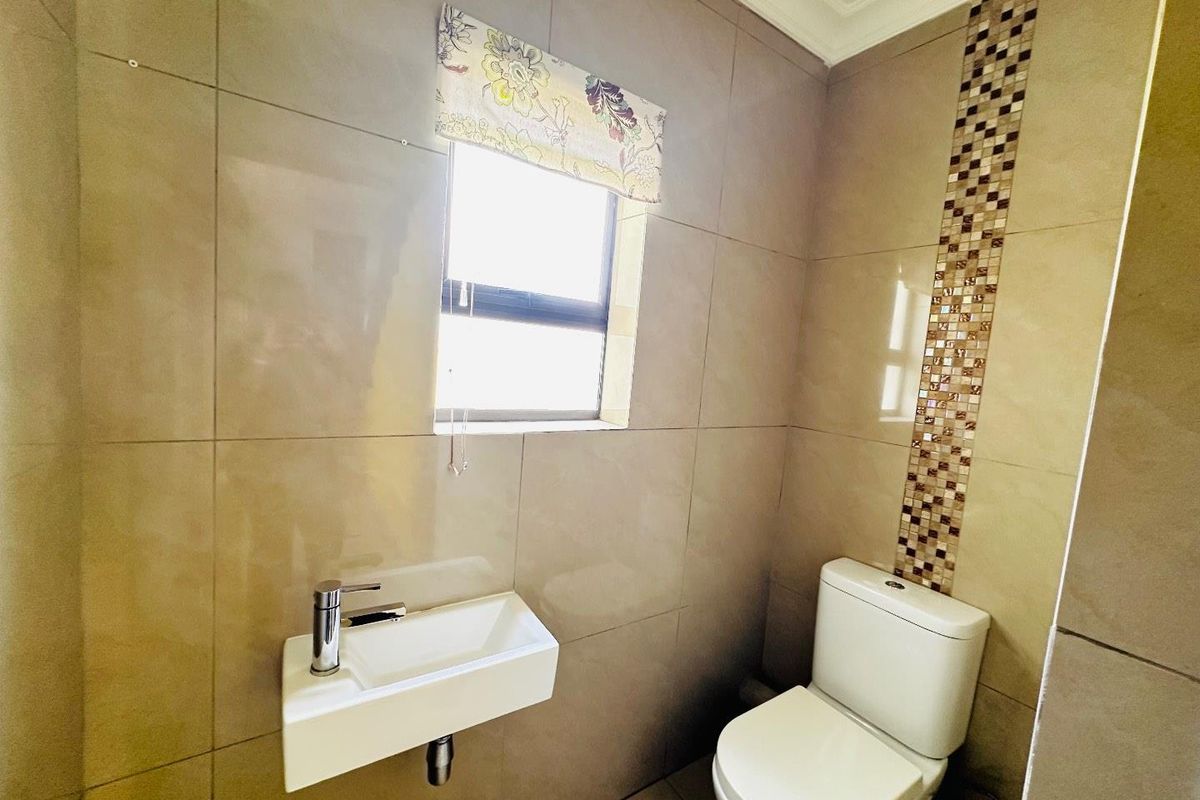 A compact guest bathroom featuring floor-to-ceiling neutral tiling, a wall-mounted basin, and a modern toilet with decorative mosaic tile accents.