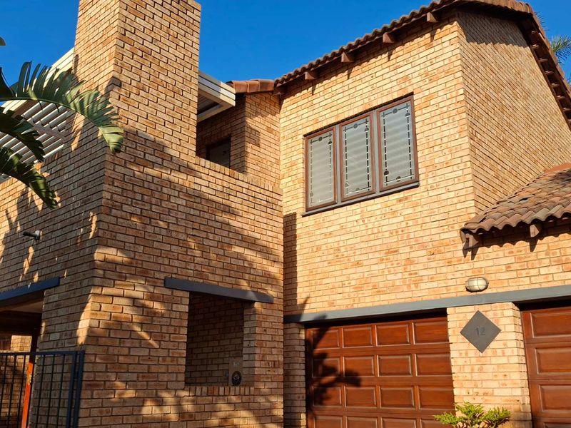 A well-maintained double-story townhouse featuring a classic face brick exterior, tiled roof, and integrated double garage.