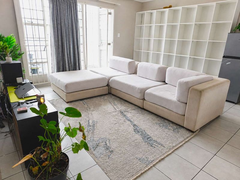 A living room featuring tiled flooring, a large built-in shelving unit, and access to a balcony through a sliding glass door with security gate.