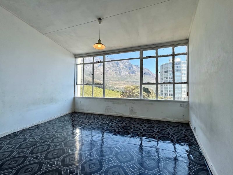 An empty living room featuring large windows with mountain views, patterned flooring, and a pendant light, requiring cosmetic updates to the walls.