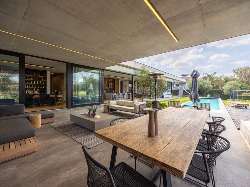 Expansive covered patio featuring a concrete ceiling with integrated lighting, large format tiling, and seamless transition to the swimming pool and garden area.