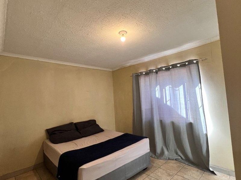 A simple bedroom featuring tiled flooring and a textured ceiling, offering a functional space ready for cosmetic updates.