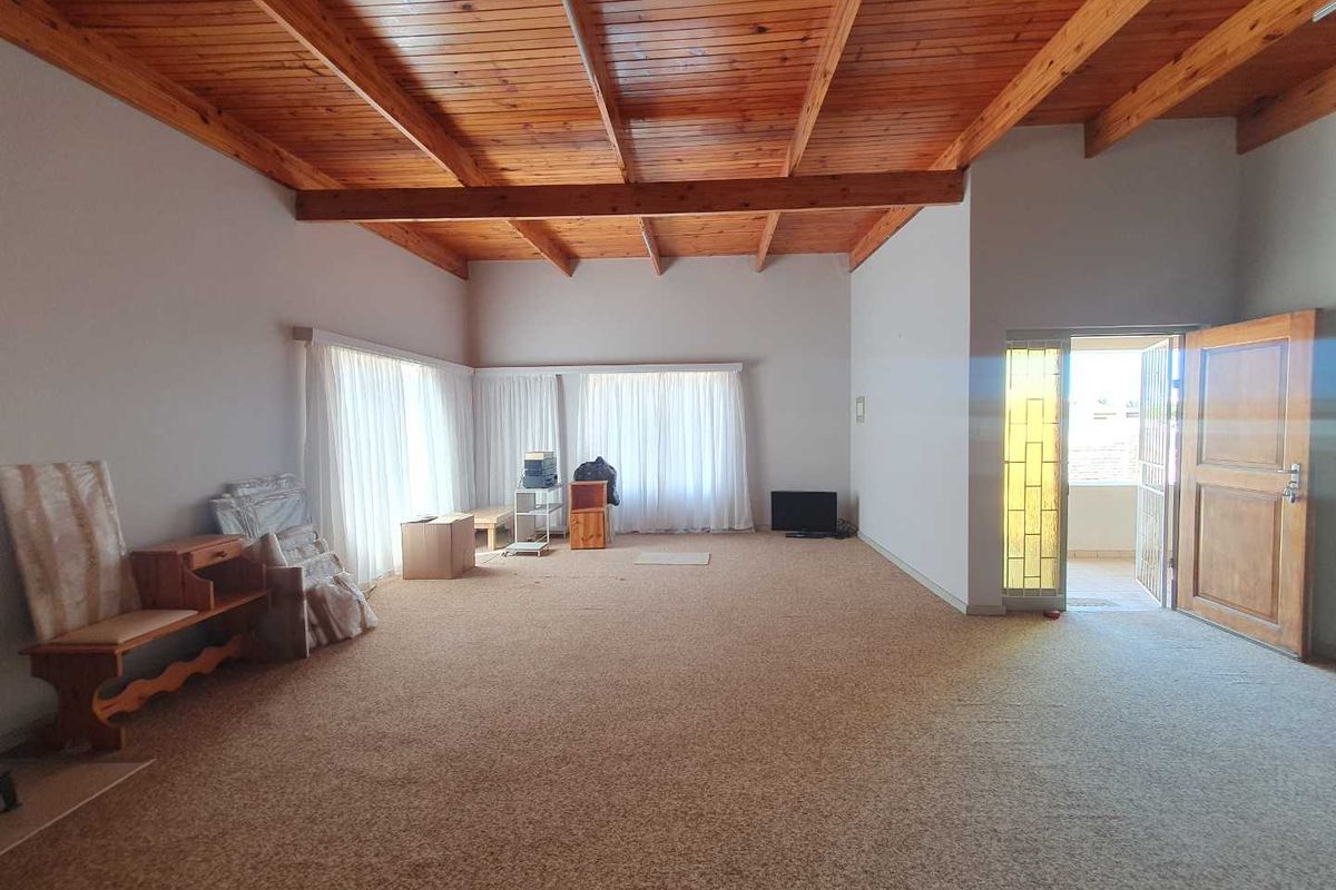 Spacious living area featuring high exposed timber beam ceilings, neutral walls, and direct access to an outdoor patio space.