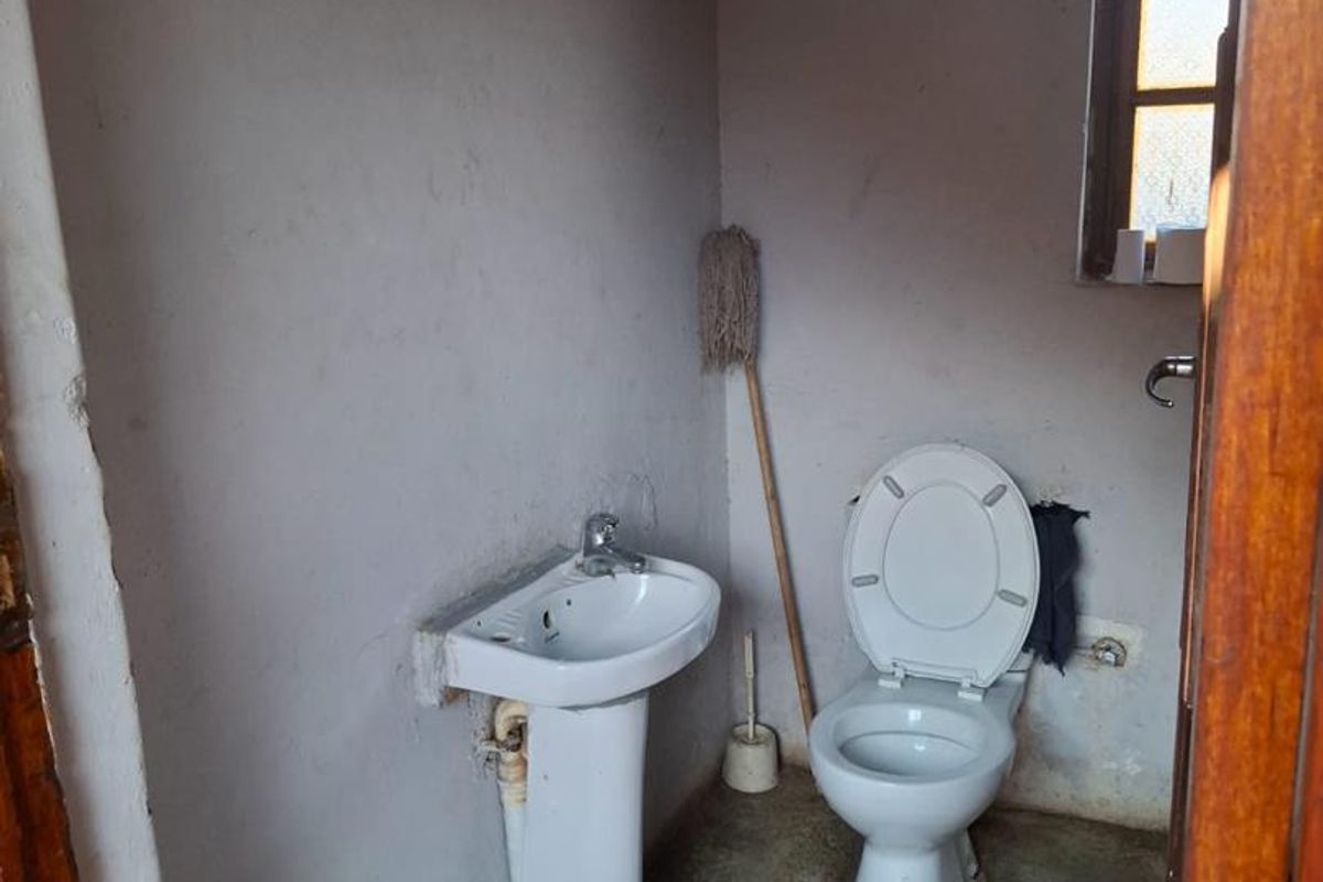 A small, basic bathroom featuring a pedestal basin and toilet, requiring significant cosmetic updates and finishing to the flooring and walls.