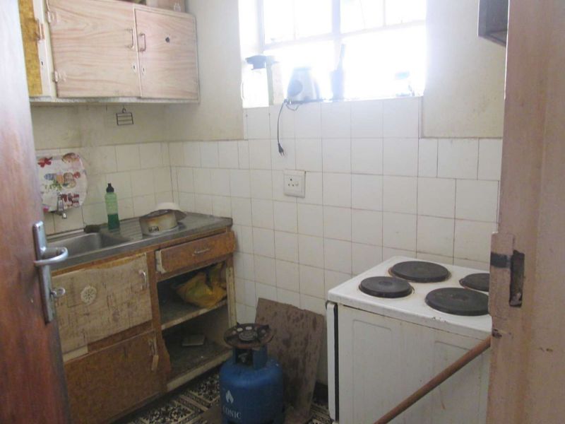A dated kitchen featuring basic cabinetry, a stainless steel sink, and a tiled backsplash, requiring significant renovation to modernize the space.