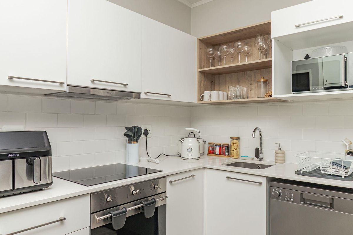 Modern kitchen featuring white cabinetry, subway tile backsplash, integrated oven, electric hob, extractor fan, and a stainless steel sink.