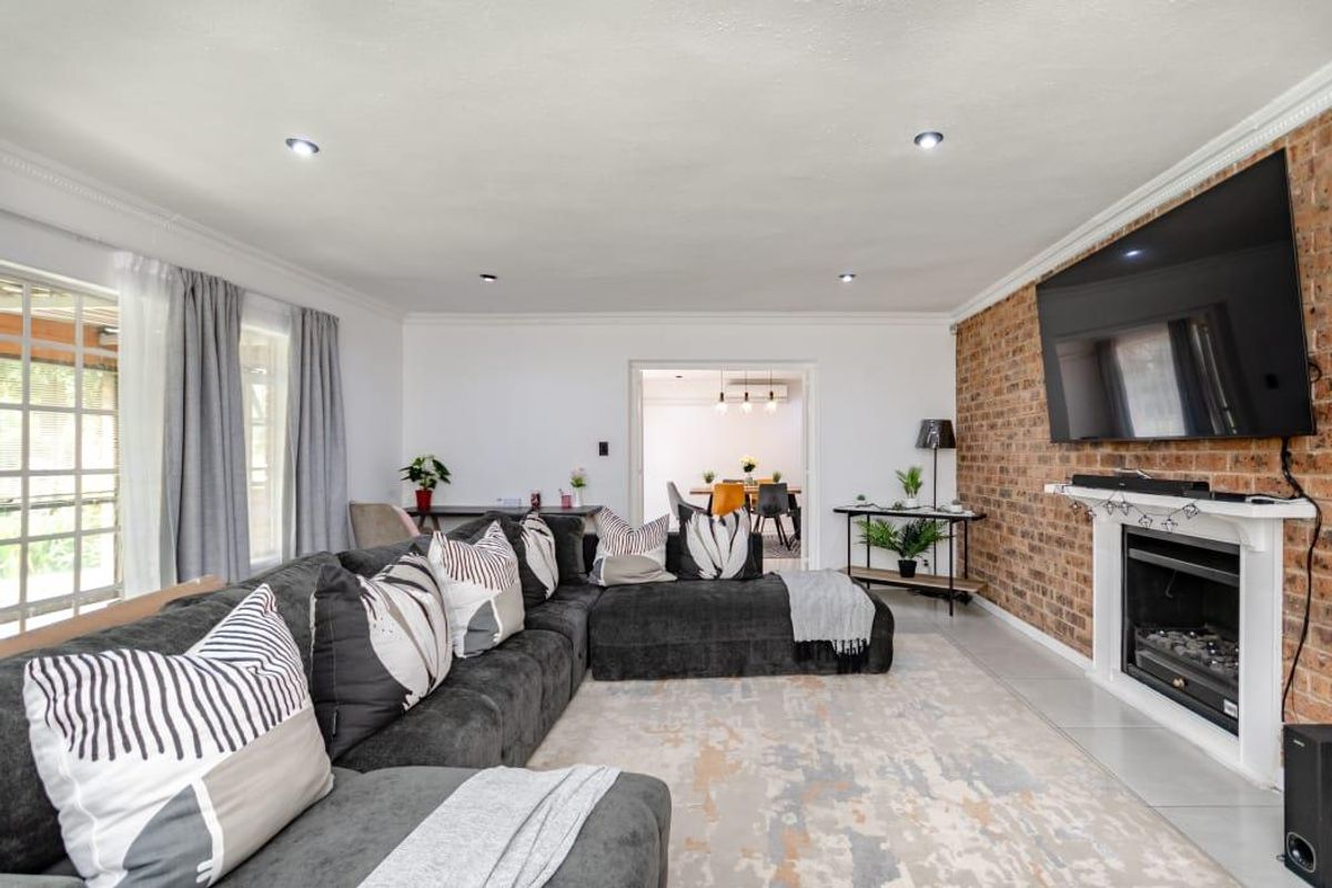 Spacious living room featuring a prominent exposed brick feature wall, a built-in fireplace, and recessed ceiling lighting, with an open flow to the dining area.