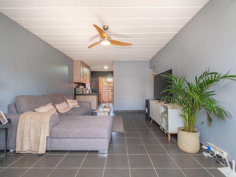 Open plan living area featuring tiled flooring, a ceiling fan, and a compact kitchen space with direct access to an exterior security gate.