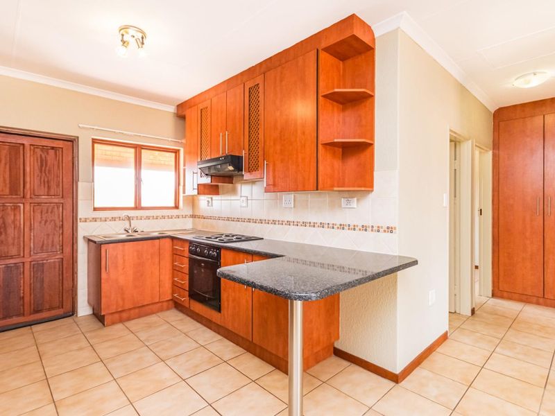 A functional kitchen featuring wooden cabinetry, granite countertops, a built-in oven with hob, and tiled flooring, offering a clean and practical workspace.