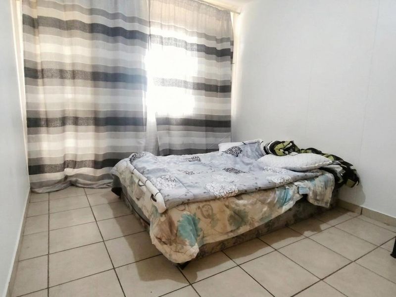 A simple bedroom featuring tiled flooring and large window curtains, providing a functional space with neutral finishes.