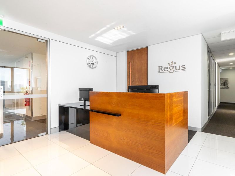 Professional office reception area featuring a built-in wooden desk, glass entry door, and clean tiled flooring in a modern corporate environment.