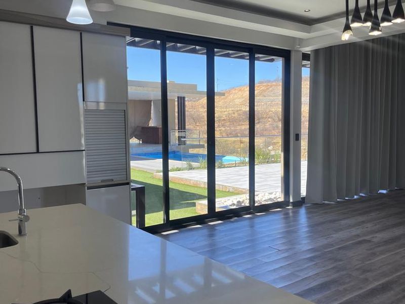 Modern open-plan kitchen and living area featuring a stone island with gas hob, recessed lighting, and large sliding doors opening to the pool area.
