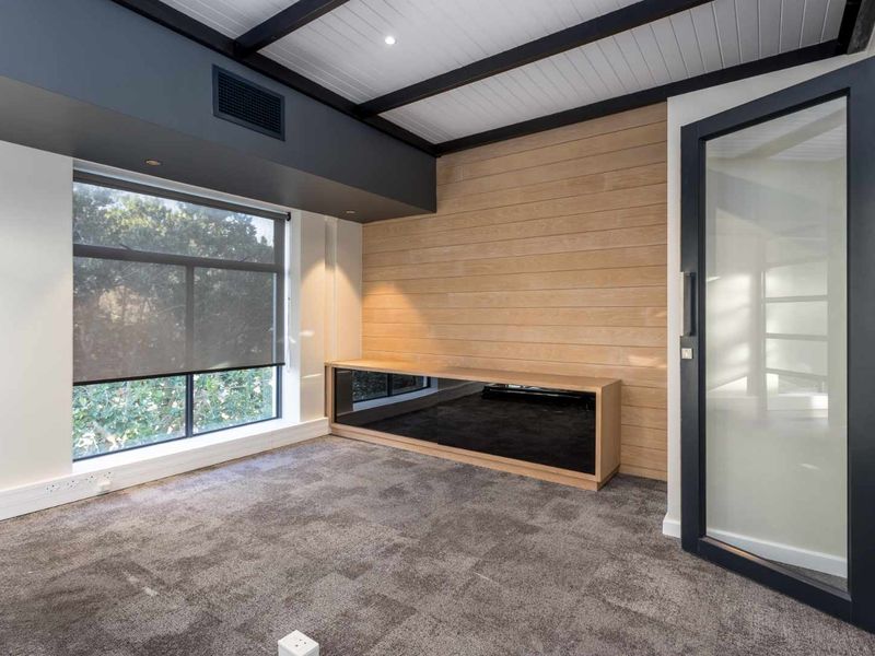 Modern office space featuring timber wall paneling, built-in cabinetry, exposed ceiling beams, and large windows with roller blinds.