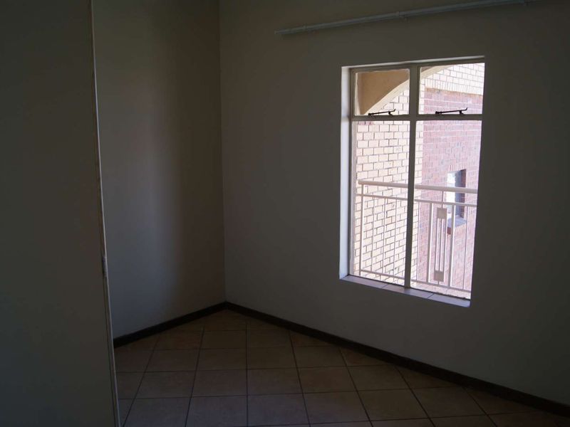 An empty bedroom featuring tiled flooring and a window with a view of the exterior brick facade.