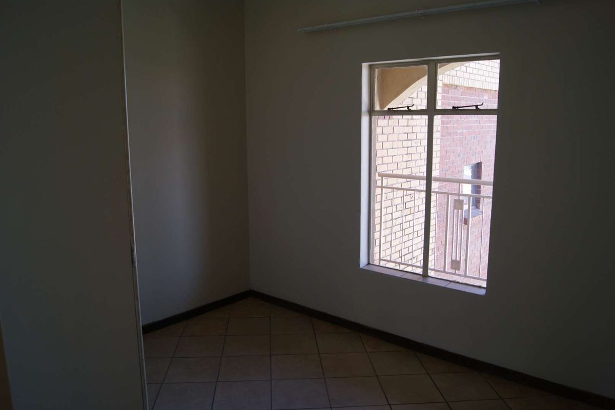 An empty bedroom featuring tiled flooring and a window with a view of the exterior brick facade.