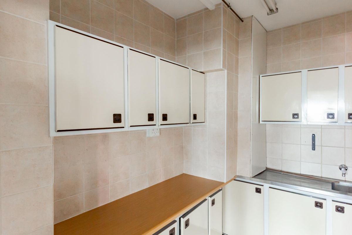 A functional office kitchenette featuring built-in cabinetry, a laminate countertop, and a stainless steel sink with wall-mounted taps.