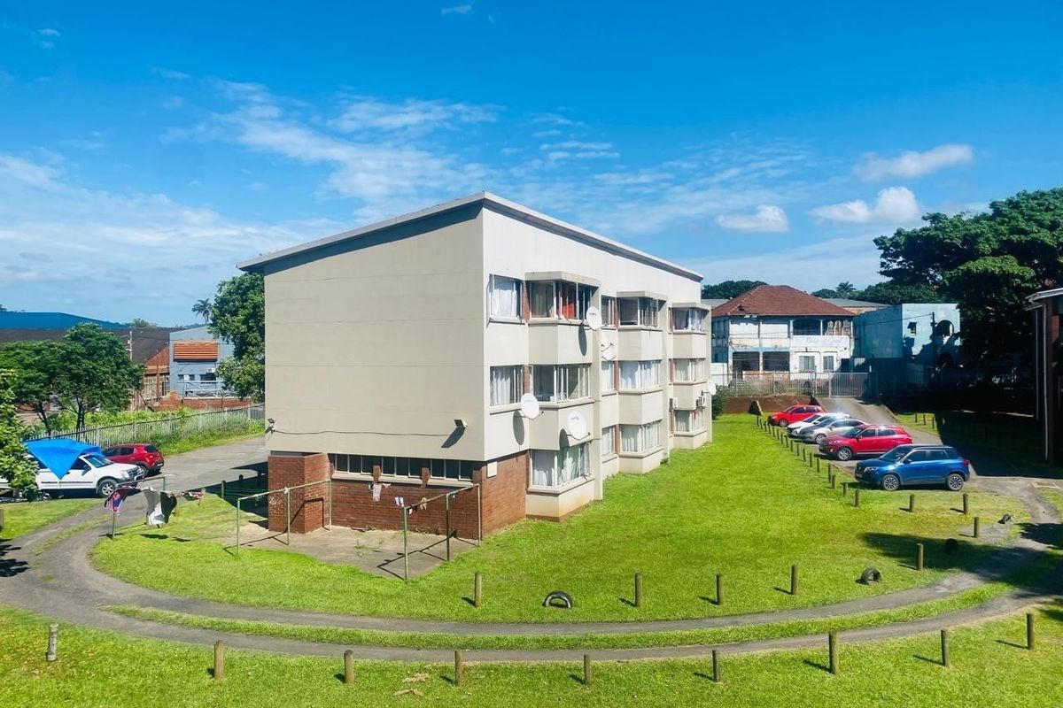 Exterior view of a multi-story apartment building featuring a brick and rendered facade, set within a communal garden area with paved access.