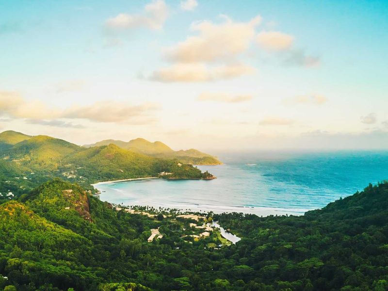 A breathtaking aerial view of the lush coastal landscape, featuring rolling green hills, a pristine beach, and the expansive blue ocean.