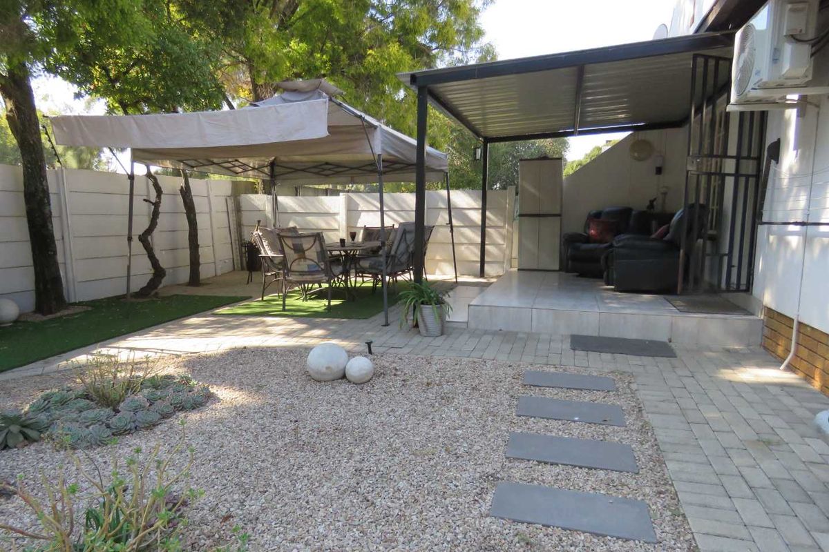 A private rear garden featuring a covered patio area, paved walkways, gravel landscaping, and a precast boundary wall.