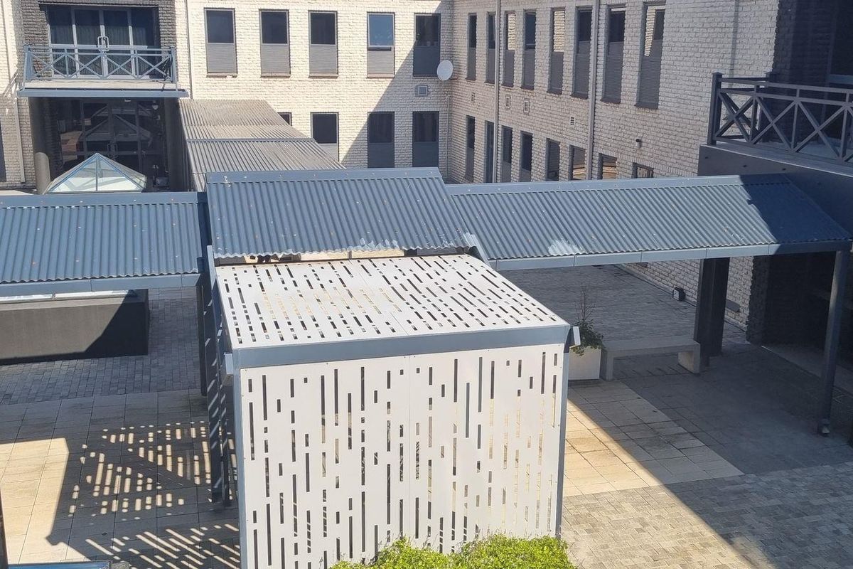 An elevated view of a modern office complex courtyard featuring paved walkways, covered metal corridors, and contemporary architectural screening.