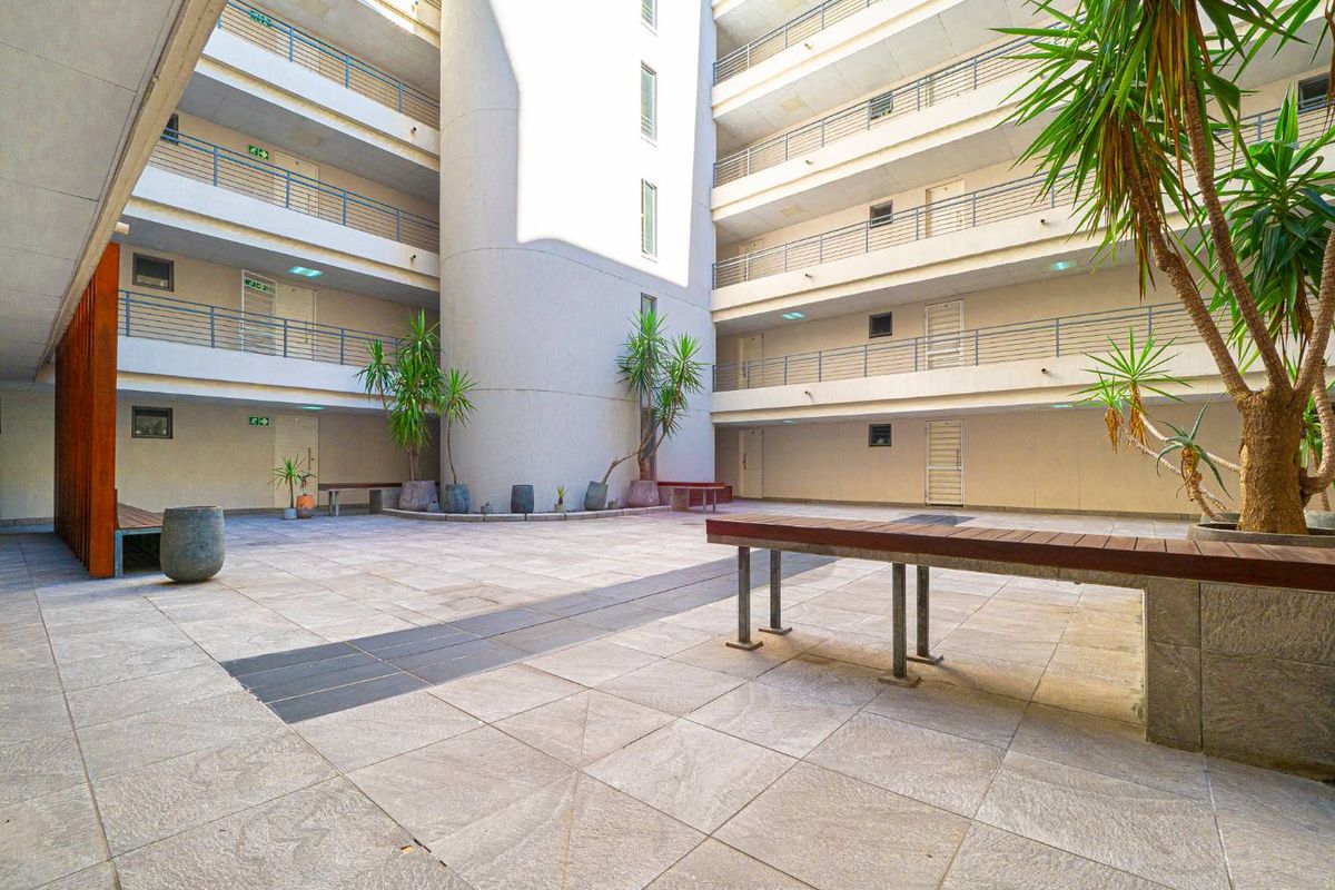 A central open-air courtyard within an apartment complex, featuring paved flooring, multi-level walkways with metal railings, and a central architectural pillar.