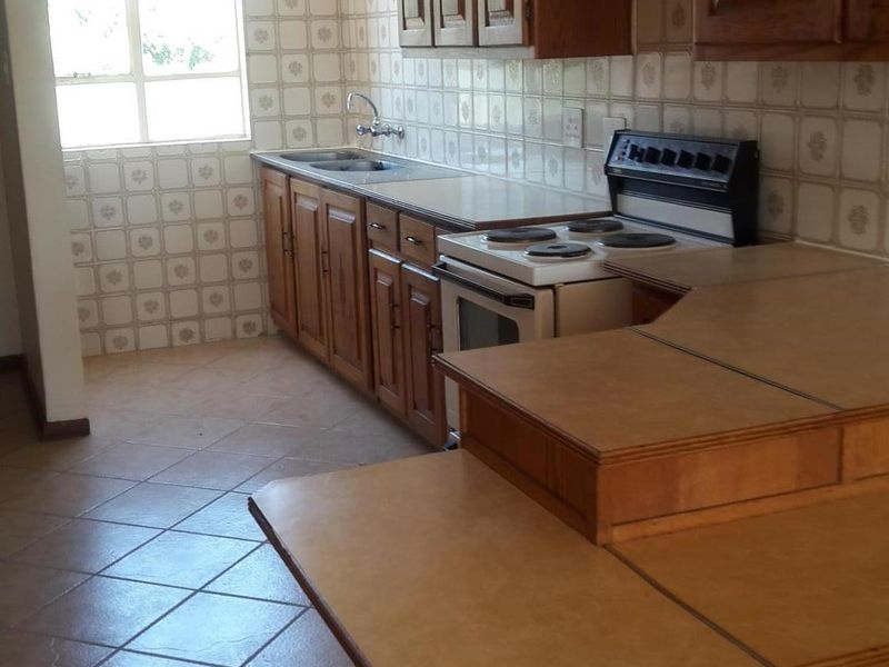 A dated kitchen featuring wooden cabinetry, laminate countertops, and ceramic tiling throughout, offering a functional layout ready for modernization.