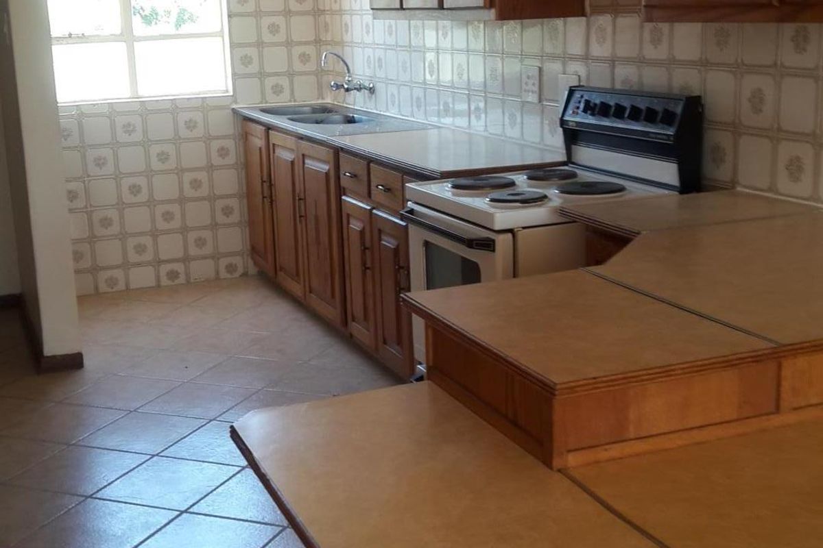 A dated kitchen featuring wooden cabinetry, laminate countertops, and ceramic tiling throughout, offering a functional layout ready for modernization.